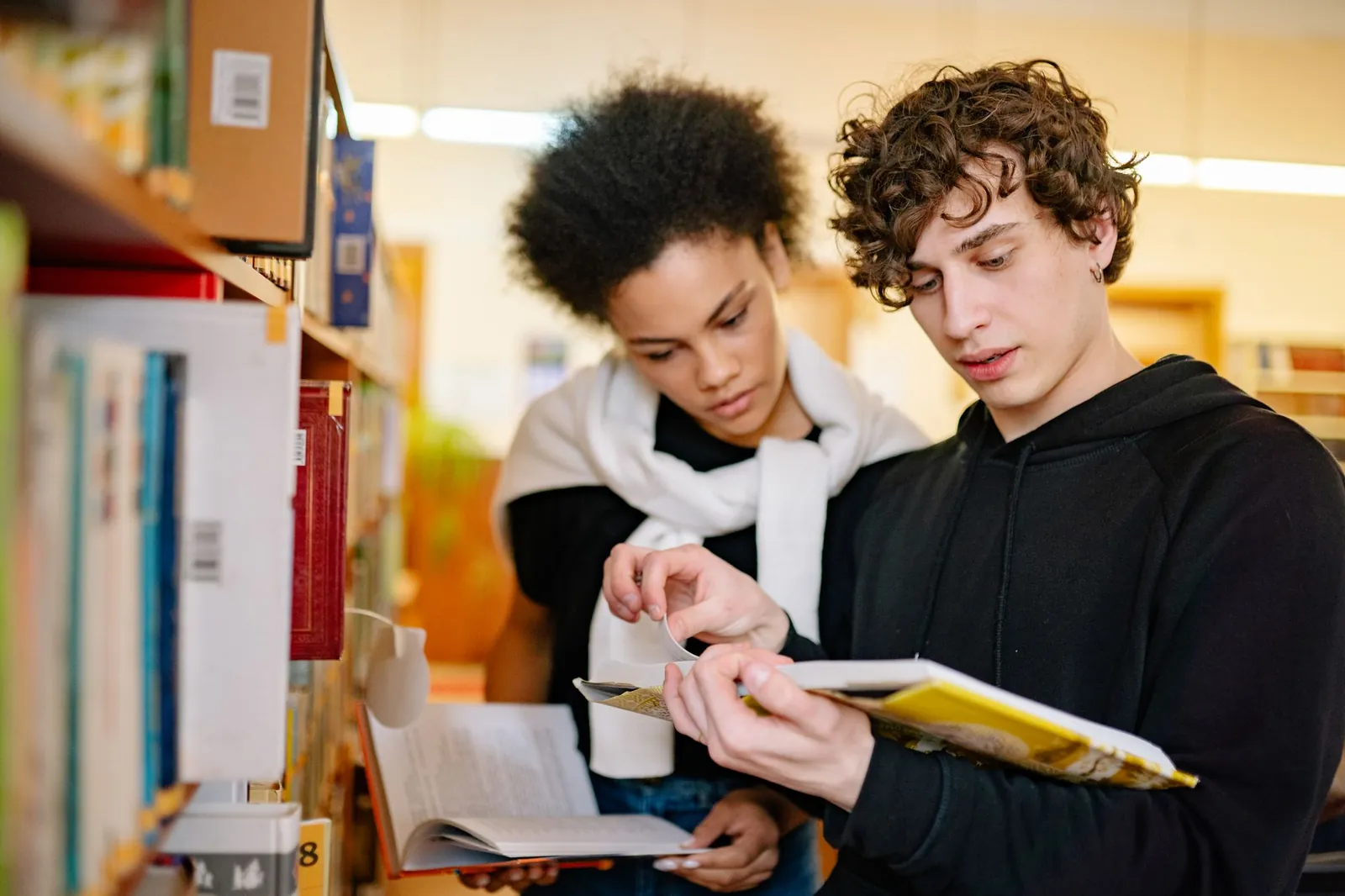 Two GCSE students reading a textbook together in a library
