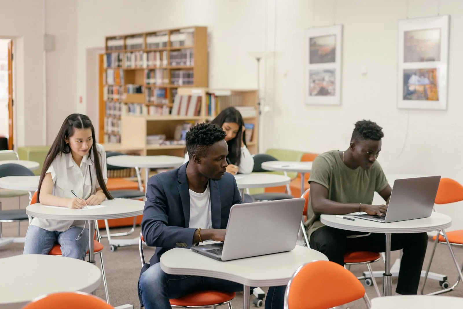 Adult learners studying with laptops and notes in a modern library